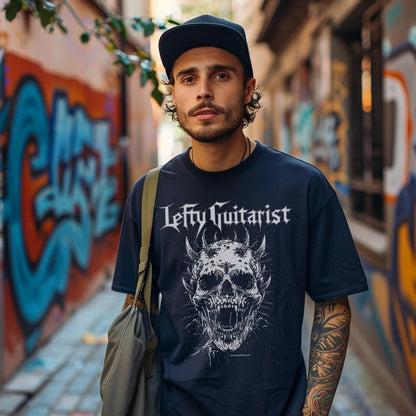 Unisex navy T-shirt featuring a horned skull graphic and "LeftyGuitarist" text, worn by a man in an urban graffiti setting.