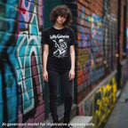 A black LeftyGuitarist "Skeleton" unisex t-shirt featuring a skeleton playing lefty guitar, worn by a woman standing in front of a graffiti background