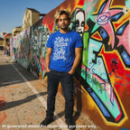 Royal blue unisex T-shirt featuring the text "Life is Better with a Lefty Bass" and a graphic of a left-handed bass guitar worn by a dyed blond haired South Asian man standing in front of a wall with graffiti.