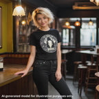 A unisex black T-shirt featuring "I Play Guitar Like Iommi" graphic, worn by a woman with short messy blonde hair in a café setting.