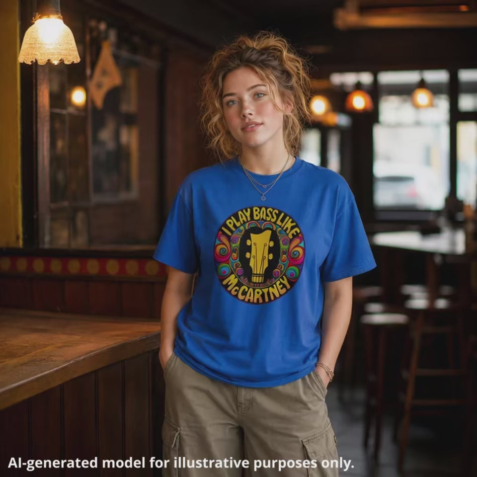 Woman wearing a royal blue "I Play Bass Like McCartney" unisex tee featuring a colorful psychedelic design with a guitar headstock silhouette.
